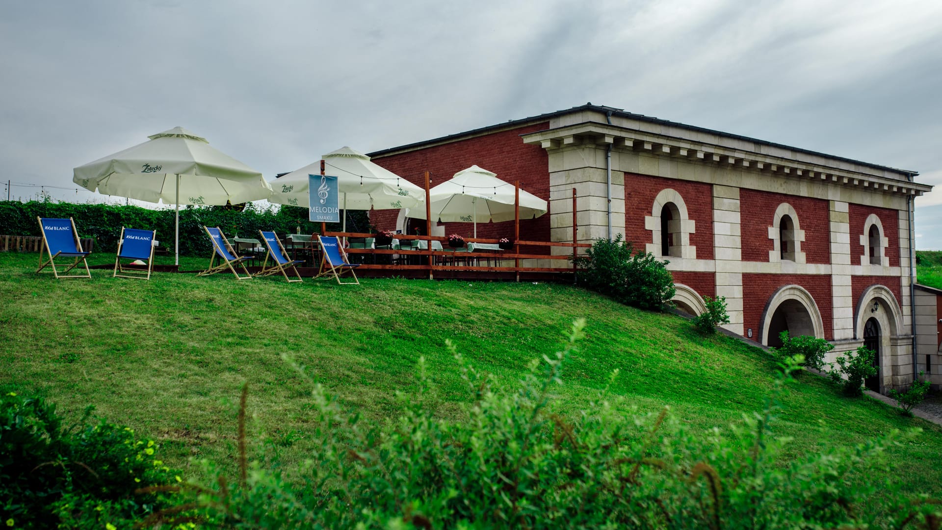 Ogród restauracji Melodia Smaku z parasolami i leżakami przed zabytkową Bramą Szczebrzeską w Zamościu